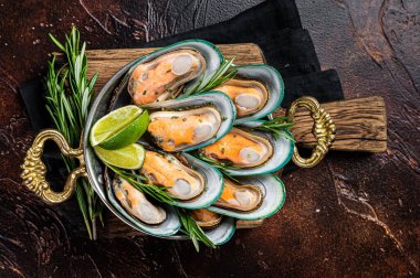 Steamed cooked Green mussels with herbs and spices in a skillet. Dark background. Top view.