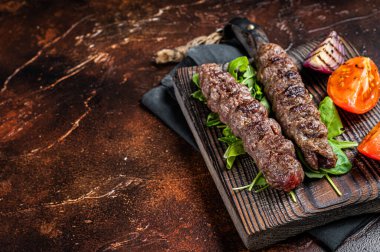 Turkish adana kebab, ground beef and lamb meat grilled on skewers served with tomato, salad and onion. Dark background. Top view. Copy space.