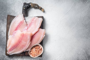 Uncooked tilapia fish fillet on a wooden board. White background. Top view. Copy space.