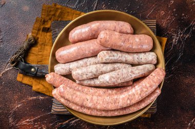 Assorted raw homemade sausages with Beef, pork, lamb and chicken meat on a plate. Dark background. Top view.