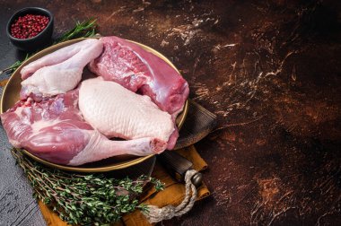 Fresh duck meat parts, raw breast steak, legs, wings in a plate with herbs. Dark background. Top view. Copy space.