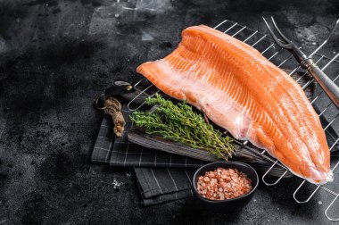 Çiğ somon balığı filetosu, ızgarada otla biftek pişirme. Siyah arka plan. Üst Manzara. Boşluğu kopyala.