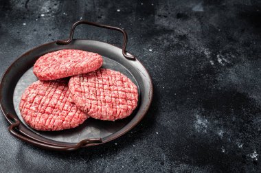 Fresh raw homemade minced beef steak burger in steel tray. Black background. Top view. Copy space.