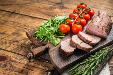 Roast Veal tenderloin, sliced Roastbeef on wooden board with garnish. Wooden background. Top view. Copy space.
