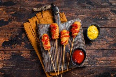 Mini Deep fried corn dogs with mustard and ketchup on wooden board. Wooden background. Top view.