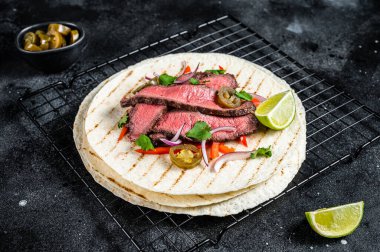 Grilled Beef steak Fajitas, taco tortillas with onion, jalapeno and bell pepper. Black background. top view.