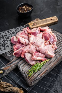 Raw chicken stomachs, giblets gizzards on a butcher board with meat cleaver. Black background. Top view.