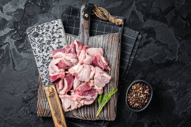 Raw chicken stomachs, giblets gizzards on a butcher board with meat cleaver. Black background. Top view.