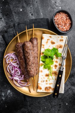 Lamb meat kofta kebab, onion and flat bread on plate. Black background. Top view.