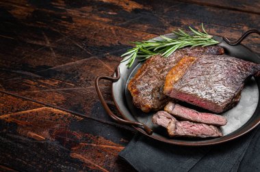 Grilled picanha or top sirloin beef steak with rosemary in steel tray. Wooden background. Top view. Copy space.