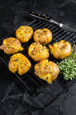 Crushed, smashed potatoes baked with rosemary and thyme. Black background. Top view.