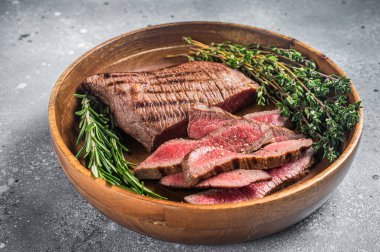 Grilled sliced Skirt Steak on a plate with herbs. Gray background. Top view.