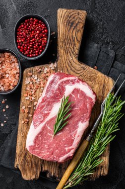 Çiğ kaburga bifteği, ahşap tahtada mermer et ve biberiye. Siyah arka plan. Üst görünüm.