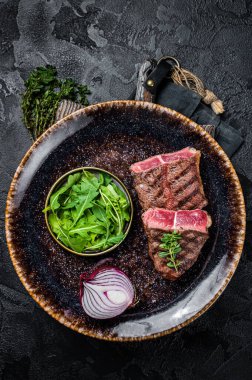 Grilled Oyster Top Blade beef meat steak on a plate with salad. Black background. Top View.