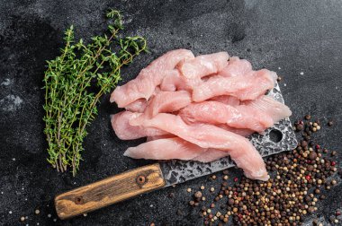 Slices of raw poultry meat on a butcher board with meat cleaver, chicken breast. Black background. Top view.