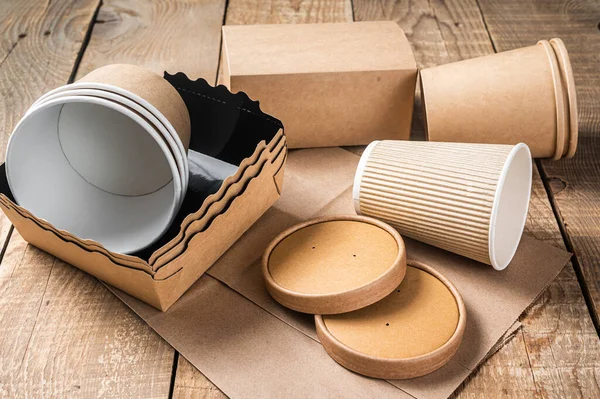 Disposable paper tableware. Eco friendly Recycling set of paper cups, dishes, bag, fast food containers and cutlery. Wooden background. Top view. Copy space.