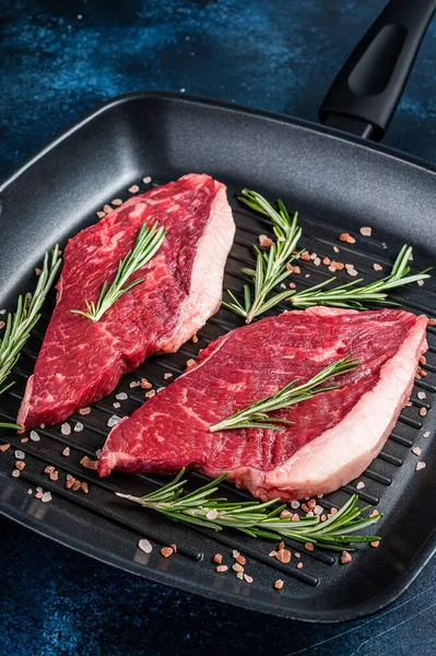 Ready for cooking raw rump or sirloin beef meat steak in a grill skillet. Blue background. Top view.