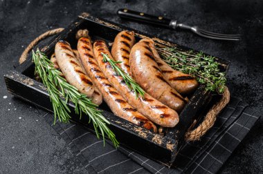 Fried on a grill skillet mix sausages in a wooden tray with herbs. Black background. Top view.
