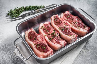 Marinated Raw meat of lamb mutton saddle in steel tray with thyme, spices and olive oil. White background. Top view.