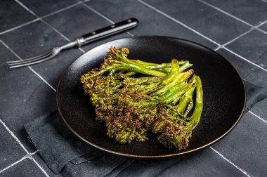 Roasted green Broccolini Sprouts with garlic butter in a plate. Black background. Top view.