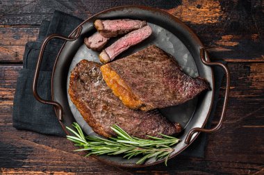 Grilled picanha or top sirloin beef steak with rosemary in steel tray. Wooden background. Top view.