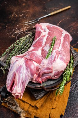 Mutton lamb whole shoulder, raw meat in a steel tray with herbs. Dark background. Top view.