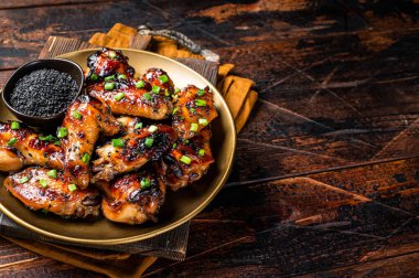 Teriyaki chicken wings with black sesame in a plate. Wooden background. Top view. Copy space.