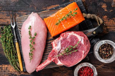 Çiğ biftekler - balık somonu, sığır eti ve kesme tahtasındaki hindi göğsü filetosu. Ahşap arka plan. Üst görünüm.