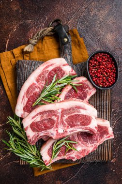 Raw fresh saddle of lamb mutton with herbs and spices on butcher board. Dark background. Top view.