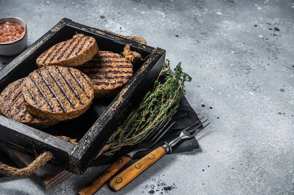 Roasted meat free patties, plant based meat burger cutlets in wooden tray with herbs. Gray background. Top view. Copy space.