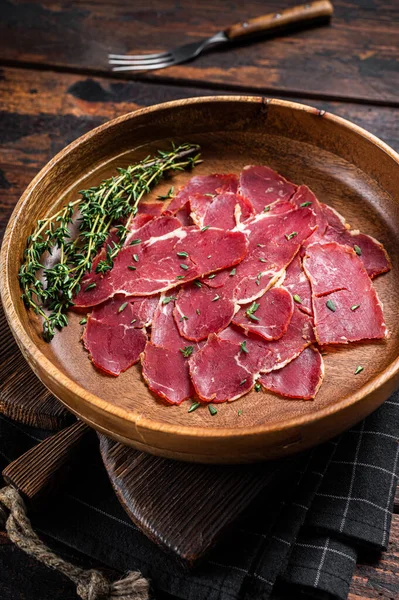 Pastrami slices, dried beef meat with herbs in wooden plate. Wooden background. Top view.