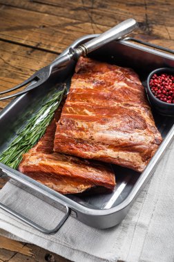 American Smoked Pork spare Ribs in steel tray with herbs. Wooden background. Top view.