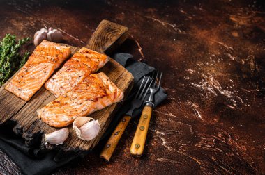 Grilled salmon fillets, fish steaks on wooden board with thyme. Dark background. Top view. Copy space.