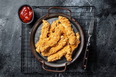Crispy chicken tenders strips with Ketchup. Black background. Top view.