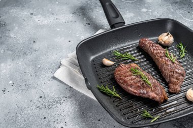 Roasted on a grill skillet Flank flap or Bavette beef meat steak with rosemary. Gray background. Top view. Copy space.
