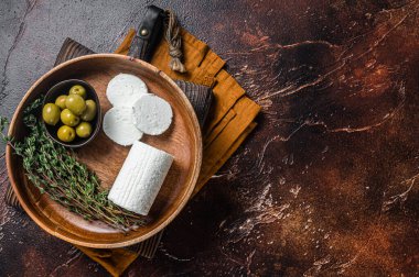 Soft Goat cheese chevre in a plate with thyme and olives. Dark background. Top view. Copy space.