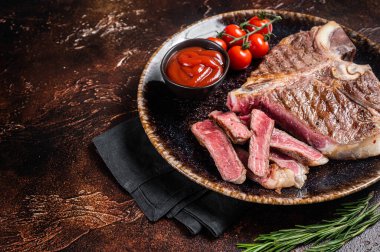 Grilled porterhouse beef meat Steak, cooked t bone in a plate with tomato. Dark background. Top view. Copy space.