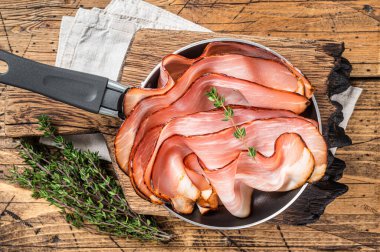 Thinly sliced German Black Forest Ham bacon in skillet. Wooden background. Top view.