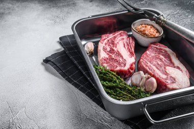 Uncooked Raw chuck eye roll steaks in a steel kitchen tray. Gray background. Top view. Copy space.