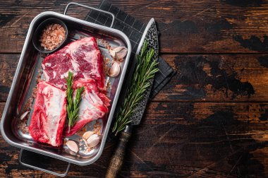 Raw beef Short Ribs in steel tray with rosemary. Wooden background. Top view. Copy space.