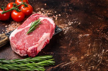 Uncooked raw Rib eye Steak, ribeye beef meat on butcher cleaver with herbs. Dark background. Top view. Copy space.