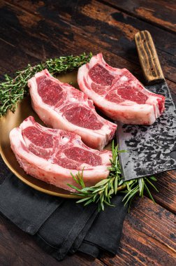 Uncooked Raw lamb loin chops steaks, saddle in plate with rosemary and thyme. Wooden background. Top view.