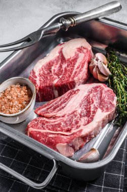 Çelik mutfak tepsisinde pişmemiş çiğ çiğ göz yuvarlama bifteği. Gri arka plan. Üst görünüm.