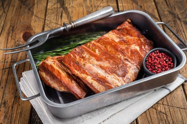 American Smoked Pork spare Ribs in steel tray with herbs. Wooden background. Top view.