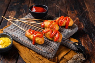 Mini Deep fried corn dogs with mustard and ketchup on wooden board. Wooden background. Top view.