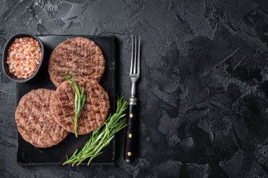 Beef burger patty cutlet for hamburger grilled on BBQ on marble board with rosemary. Black background. Top view. Copy space.