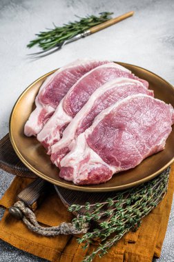 Fresh raw pork cutlet or chop steak on a plate with herbs. White background. Top view.