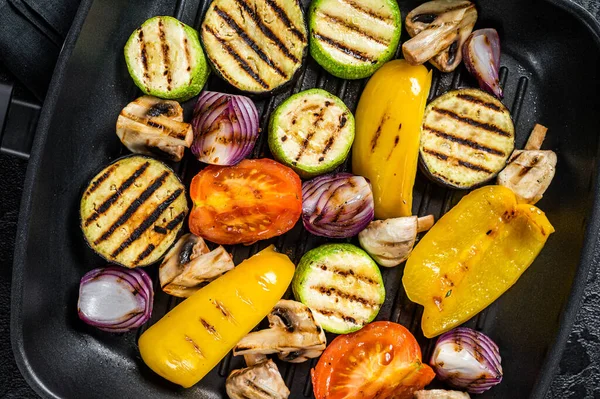 Vegetables grilled in a grill skillet, bell pepper, zucchini, eggplant, onion and tomato. Black background. Top view.