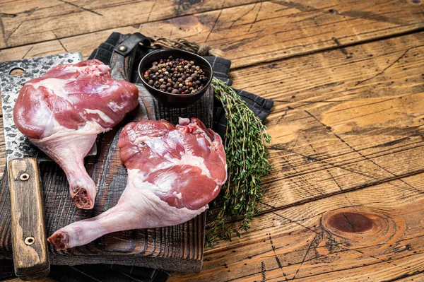 Raw duck legs with spices and chef cleaver on a wooden board. Wooden background. Top view. Copy space.