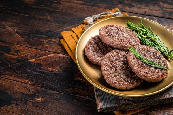 Grilled burger beef meat patty with herbs and spices on steel plate. Wooden background. Top view. Copy space.